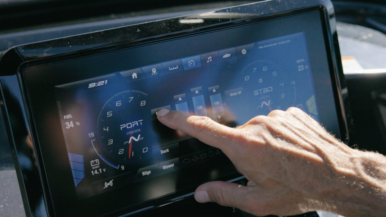 Hands on a boat’s instrument panel, showing digital gauges and steering controls.